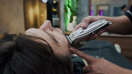 Spezialist verwendet Trimmer, um Kunden im Barbershop den Bart zu rasieren