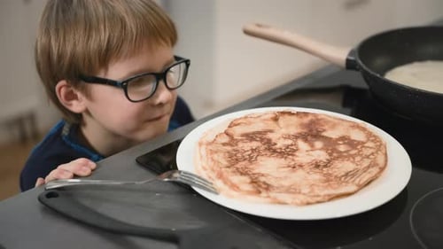A Little Boy Stealthily Takes a Pancake From a Plate on the Stove Big Closeup Slow Motion