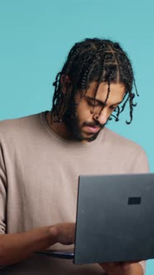 Vertical Video Man Inputting Data on Laptop While Standing in Blue Studio Background