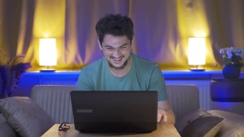 Smiling Young Adult Using Laptop at Home at Night