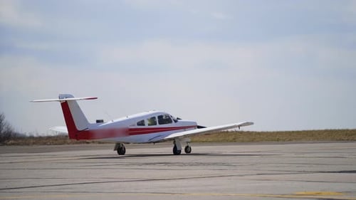 Ein kleines weißes Flugzeug mit roten Linien fährt den leeren Flugplatz ab. Das Flugzeug hebt ab.