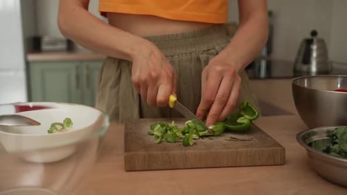 Woman Slicing a Vibrant Green Bell Pepper on a Rustic Wooden Cutting Board in a Cozy Kitchen