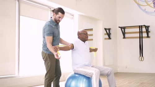 Physiotherapist Helping Patient with Resistance Band Exercises in Gym Adult