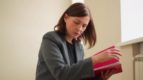 Businesswoman Organizing Papers Into Red Folder in Office Environment