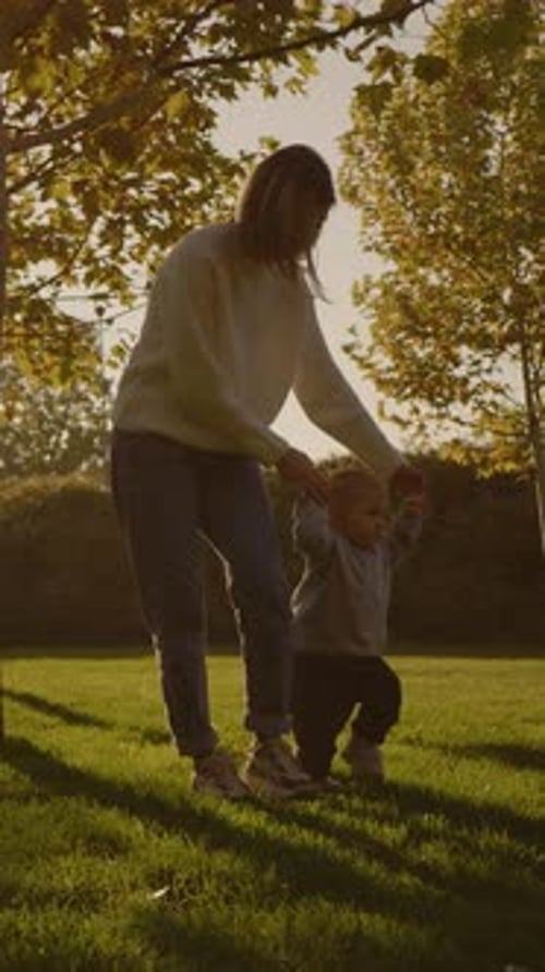 Mother Helping Toddler Learning to Walk in Park