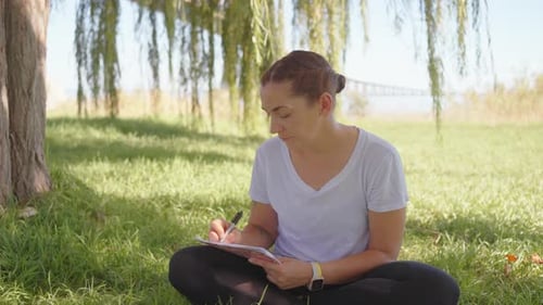 Woman with Pen Writing Sitting in Park on Nature