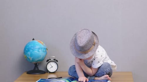 Boy Sits Reading Book with Globe and Clock