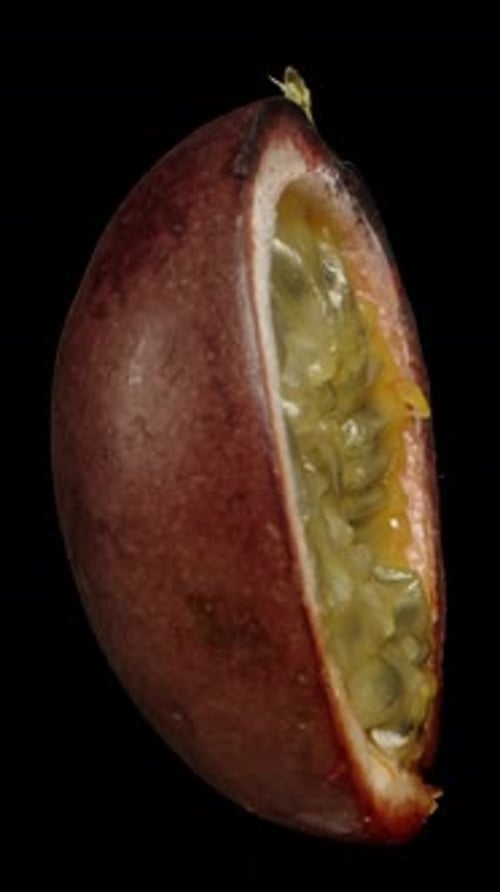Vertical video. A half of a passion fruit rotates on a black background, showcasing its side