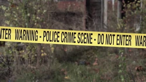 Police Crime Scene Tape in Front of Old Rustic Building and Overgrown Yard