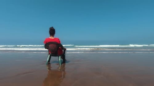 Girl in red sitting on a plastic chair on the beach of Casablanca. Subjected in the left side of the