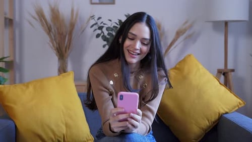 Smiling Woman Using Smartphone on Couch Indoors