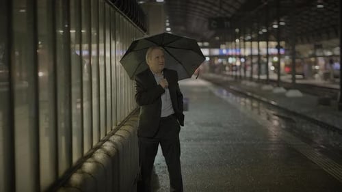 Businessperson with Umbrella on Rainy City Street Lights Reflecting in Solitude