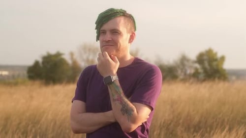 Young Thoughtful Man with Green Dreadlocks with Doubt Glance Scratching Chin in Countryside on Eve
