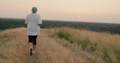 An Elderly Woman Runs Along a Country Road Goes in for Sports Rear View Active Seniors