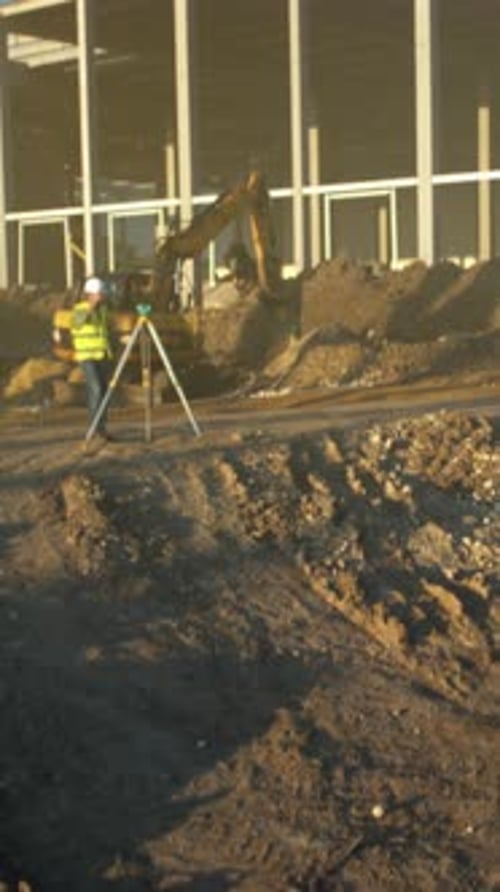 Professional Surveyor Analyzing Foundation Structures Near Heavy Machinery at Sunrise for Building