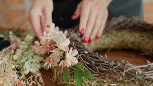 Hands of Florist Arranging Pink Flowers with Green Leaves on Rustic Twig Wreath