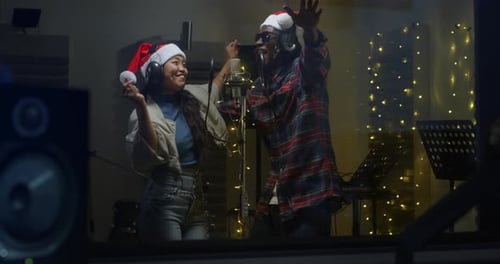 Portrait of Two Multiethnic Professional Singers in a Recording Studio, Wearing Santa Hats, Singing