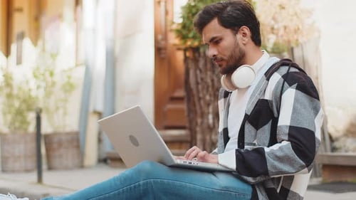 Indian Young Man Freelancer Sitting on Street Using Laptop Typing Working Online Distant Job Outdoor
