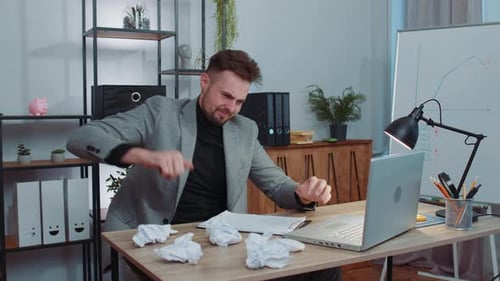 Wütender wütender Mann, der im Home Office arbeitet und zerknittertes Papier wirft mit Nervenzusammenbruch bei