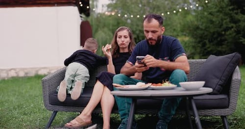 Balancing Remote Work and Family Time, Dad Engaging with Phone during Outdoor Patio Meal