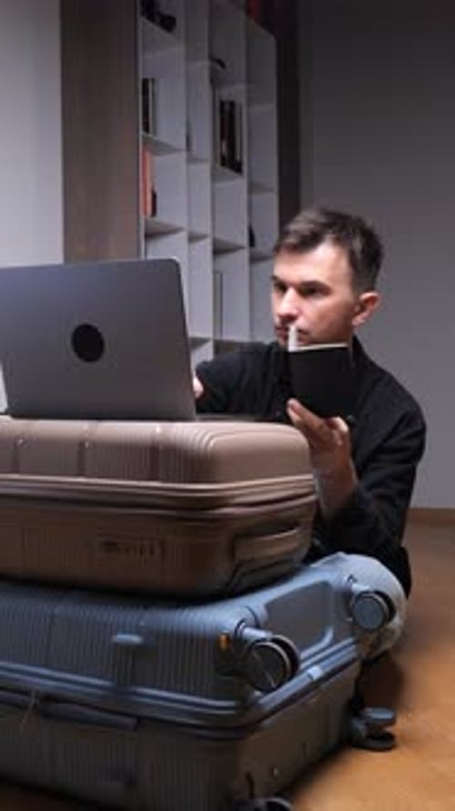 Man Works on Laptop Sitting near Luggage at Home