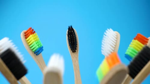 Wooden Toothbrushes with Colorful Bristles Rotating Against Blue