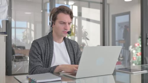 Young Man with Headset in Call Center Working on Laptop