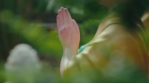 Close-up of the clasped hands of a Buddhist sitting and reciting Buddha's name, surrounded by leaves