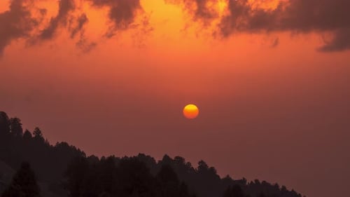 timelapse of a big orange sun descending over the mountains.