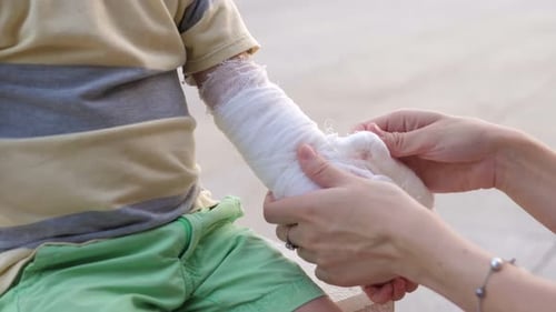 Young Mother Comforting Her Little Son and Giving Him Bandage in a Wounded Hand After Getting Hurt