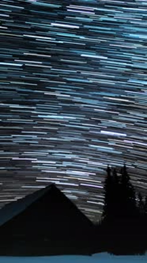 Rotating Star Trails Above Snowy Cabin at Night