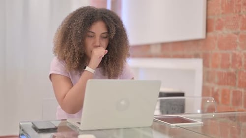 Young Woman Coughing While Working on Laptop Indoors
