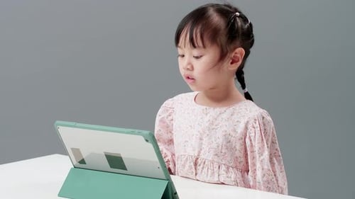 Child using digital tablet sitting near the table to watch cartoon. Record held in a studio with a g