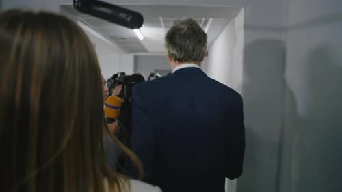 Man Surrounded by Press in Hallway