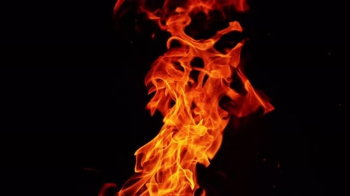 Longue flamme de feu qui s'étend dans l'air dans la nuit noire. De fines étincelles brillent dans l'obscurité.