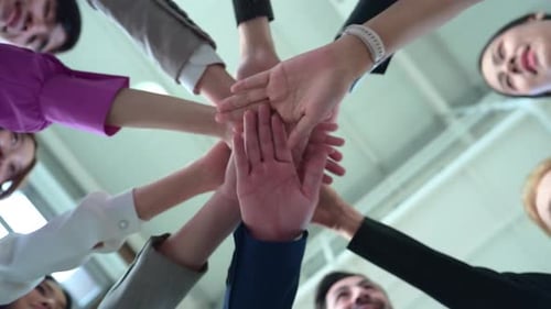 Under view of group of business people joining hands together in office to empower each other