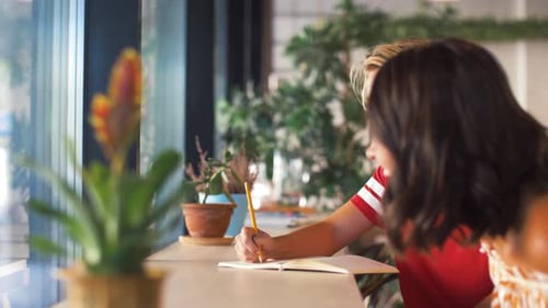 Concepto de gente y amistad: mujer joven con una amiga dibujando en un cuaderno en un café