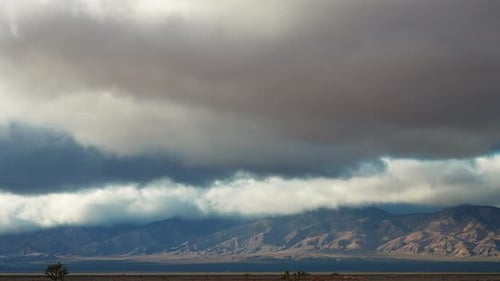 Dramatic sky over mountain range with desert land in the foreground, timelapse