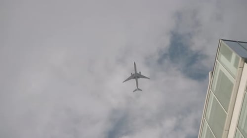 Airplane Flying In The Sky With White Clouds Over City Buildings In Tokyo, Japan. - low angle