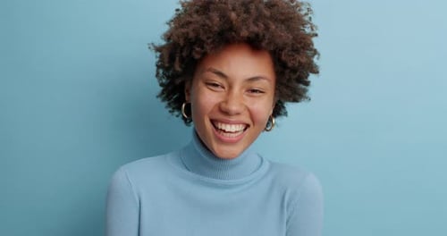 Smiling Woman in Blue Turtleneck Against Blue Background