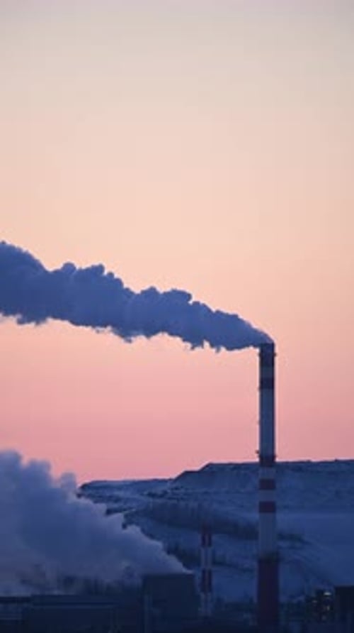 Smoke from factory pipes against the backdrop of the sunset sky.