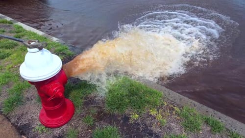 Eine Tiefwinkelaufnahme eines rot-weißen Hydranten, der an einem sonnigen Tag rostiges Wasser auf die Straße sprüht