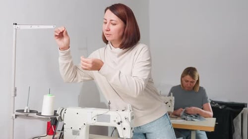 Woman Seamstress Fixing White Thread On Electric Sewing Machine In Busy Workshop
