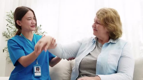 Young nurse physiotherapy with elderly patient while stretch hands in living room at home.