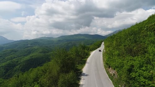 Aerial Drone Overhead of Single Car Driving Down Curvy Mountain Road Through Green Forest Valley