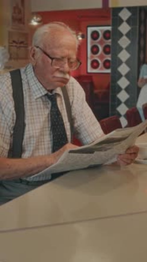 Senior Man Reading Newspaper at Table Indoors
