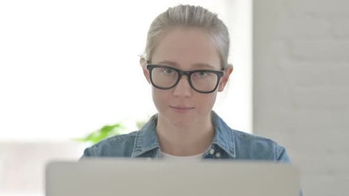 Close Up of Young Woman Looking at Camera While Using Laptop