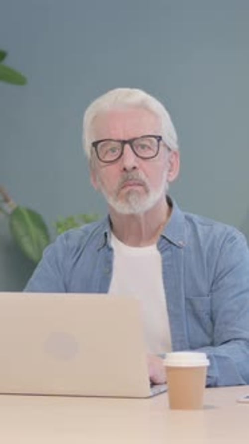 Senior Man Works on Laptop at Desk with Coffee