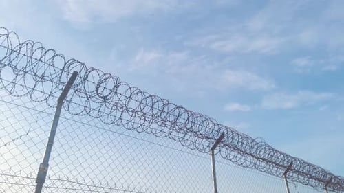 Low angle view of airport barbed wire security round metal fence on bright blue sunny sky day, handh