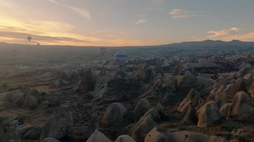 Drone view of a large hot air balloon flying very low over the rocks of Cappadocia at sunrise with G